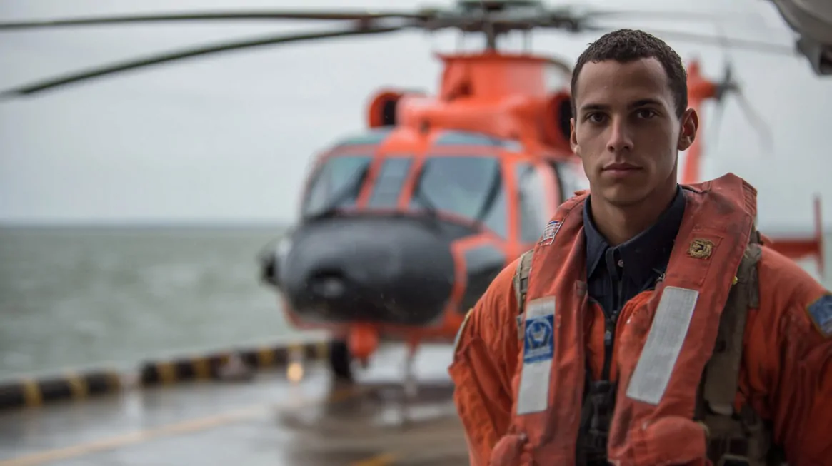 Coast Guard Reserve member standing in front of a rescue helicopter on a rainy day