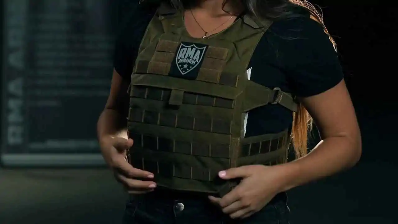 Woman adjusting a green bulletproof vest with an RMA Armament logo, showcasing the vest's features and design