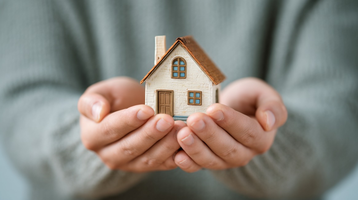 Close-up of hands gently holding a small model house, symbolizing housing security