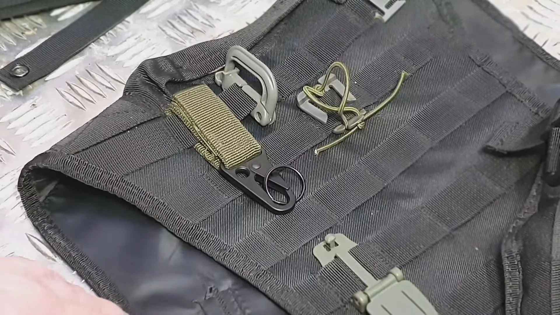 Close-up view of various attachment mechanisms on black MOLLE webbing, including buckles, clips, paracord loops, and a D-ring