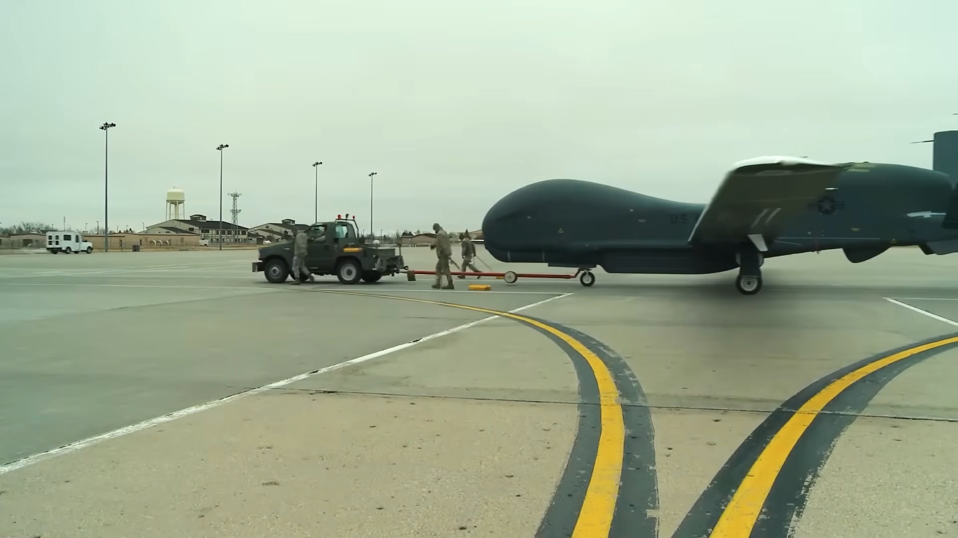 U.S. military personnel towing an RQ-4 Global Hawk drone on an airfield with a vehicle