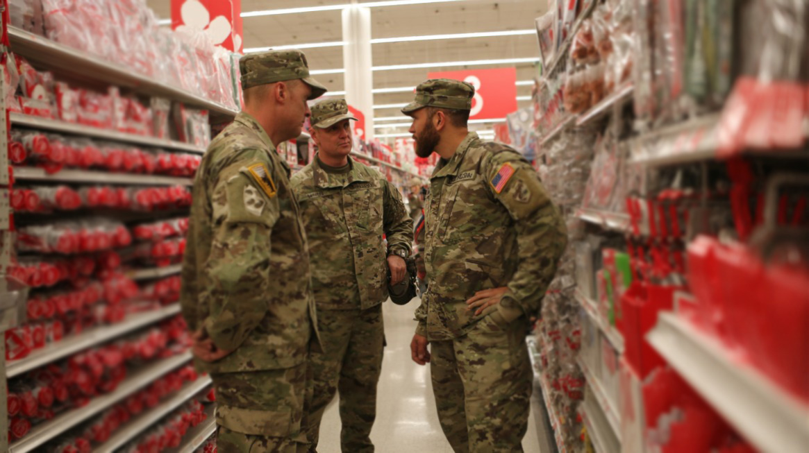 Three U.S. military personnel in uniform talking while shopping in a store aisle filled with red merchandise
