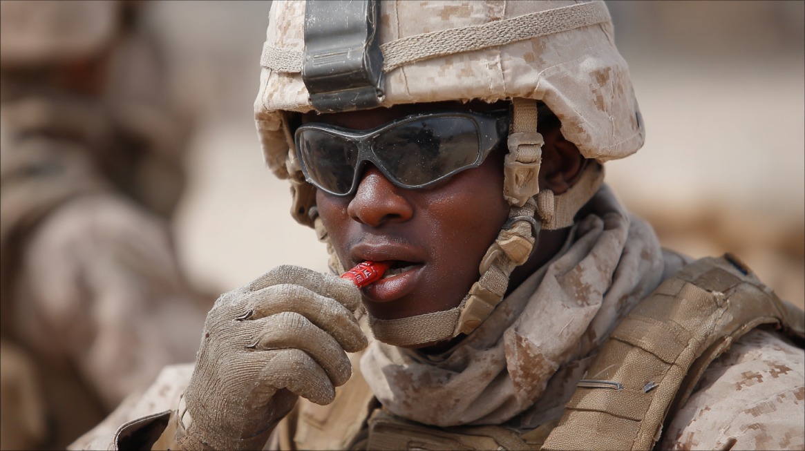 Marine in uniform and helmet with sunglasses playfully biting a red crayon