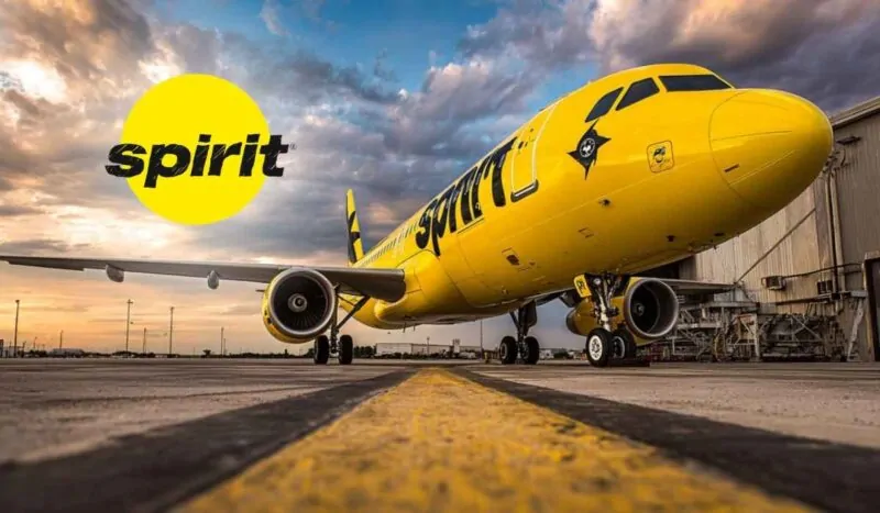 A Spirit Airlines bright yellow airplane on the runway at sunset, with the Spirit Airlines logo in the sky