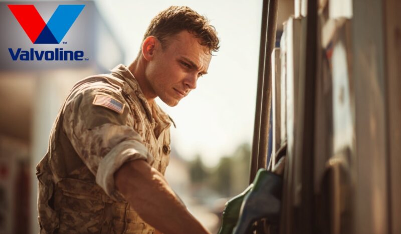 U.S. soldier in camouflage uniform refueling a vehicle at a gas station, Valvoline logo in the corner